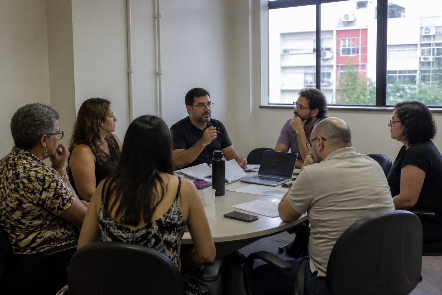 Reunião de professores e técnicos, com o campus visto pela janela